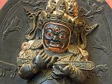 British Museum Top 20 Buddhism 13 Mahakala 13. Mahakala � Tibet, 17C AD. This stone stele shows the dharmapala (protective figure) Mahakala as Lord of the Tent, an appropriate role given the nomadic lifestyle of many Tibetans. The garland of skulls, his fierce expression and the prone male figure being trampled underfoot all add to his terrifying appearance. These symbolize his ability to destroy all impediments to enlightenment. Mahakala holds in the crooks of his arms the long wooden sounding board used to summon monks to assembly.  The half-bird, half-man figure of the Hindu deity Garuda is shown alongside Mahakala. In Mahakala's head-dress is his parent Buddha, Akshobhya, the Tathagata Meditation Buddha of the East.